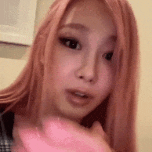 a woman with pink hair is holding a pink object in her hand and looking at the camera .