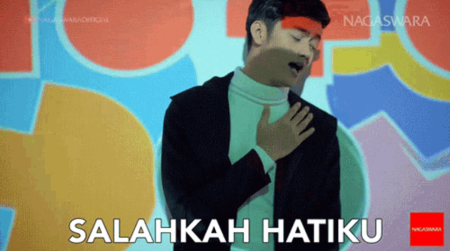 a man in a suit and white turtleneck sings salahkah hatiku in front of a colorful background
