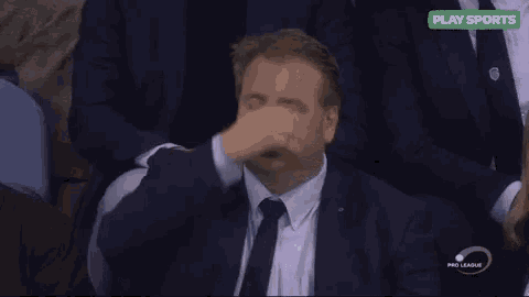 a man in a suit and tie is sitting in a stadium and making a face .