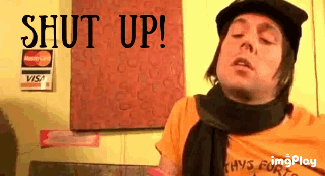 a man wearing a hat and scarf says shut up in front of a visa sign