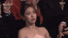 a woman in a pink dress is sitting in a crowd of people and making a face .