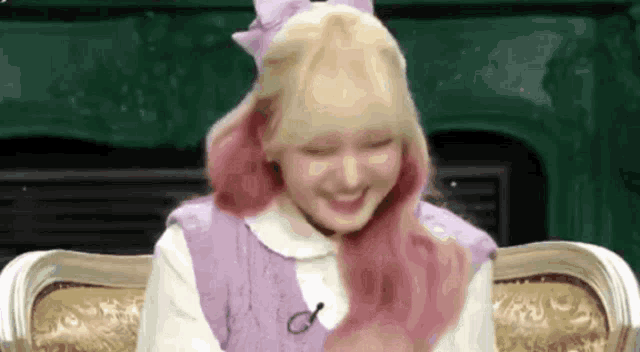 a girl with blonde and pink hair is sitting on a couch .