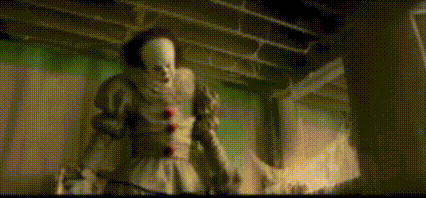 a clown is standing in a dark room holding a sword .