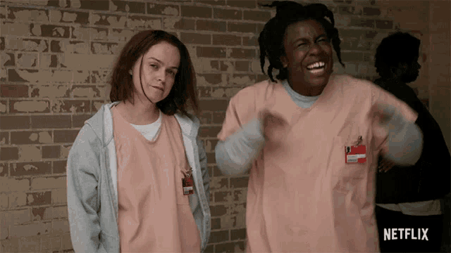 two women standing next to each other in front of a brick wall with netflix written on the bottom right