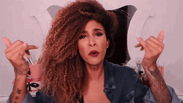 a woman with curly hair is making a heart shape with her fingers