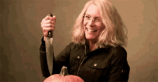 a woman is holding a knife in front of a pumpkin .