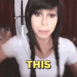 a woman with braids is wearing a white shirt and the word this is on her chest .