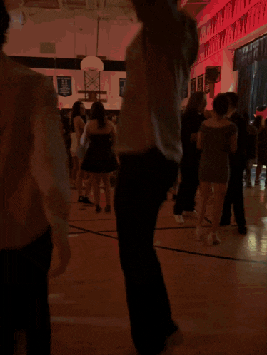 a group of people are dancing in a gym with a basketball hoop behind them