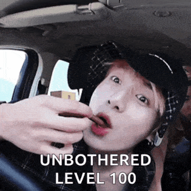 a man in a hat is eating something in a car with the words unbothered level 100 on the bottom .