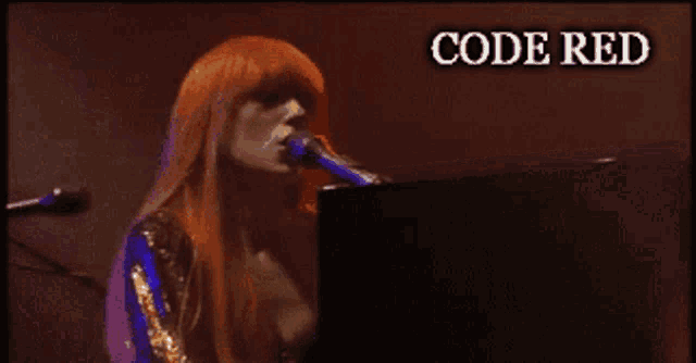 a woman singing into a microphone while playing a piano with the words code red above her