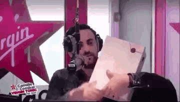a man is sitting in front of a microphone in a radio studio holding a piece of paper .