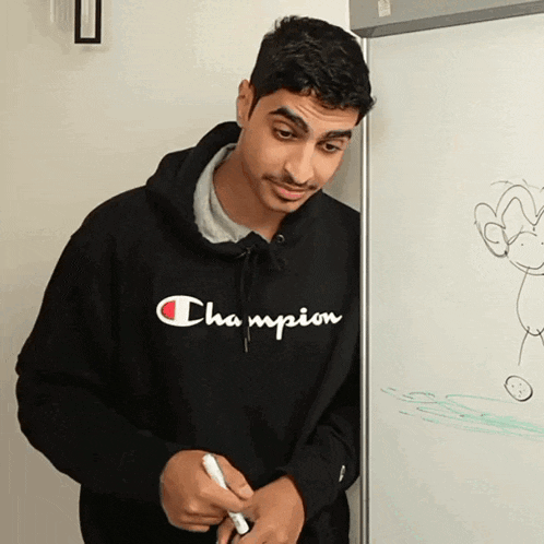 a man wearing a black champion hoodie is standing in front of a white board
