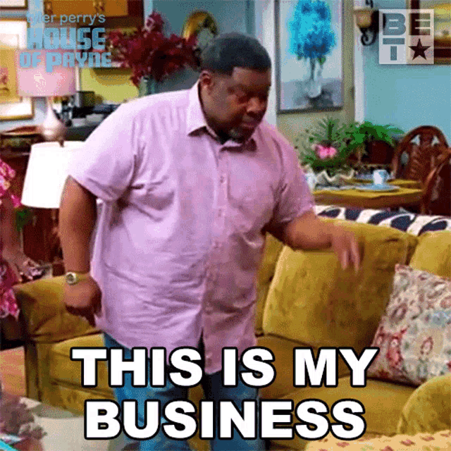 a man in a pink shirt is standing in front of a yellow couch and says " this is my business "