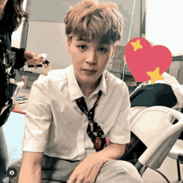 a man in a white shirt and tie sits in front of a red heart