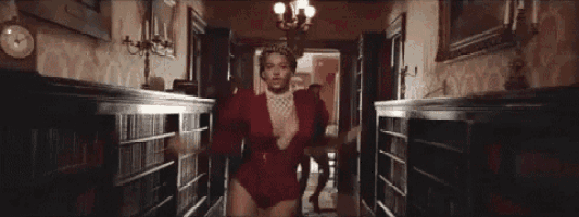 a woman in a red bodysuit is walking down a hallway next to a man .