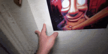 a person 's hand is reaching for a picture of a clown on the wall