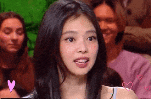 a woman with long black hair is sitting in a crowd of people and looking at the camera .