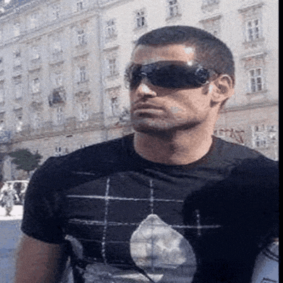 a man wearing sunglasses and a black shirt is standing in front of a building .