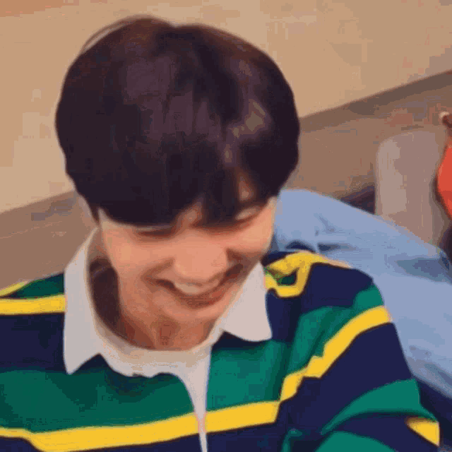 a young man wearing a striped shirt is smiling while sitting down .