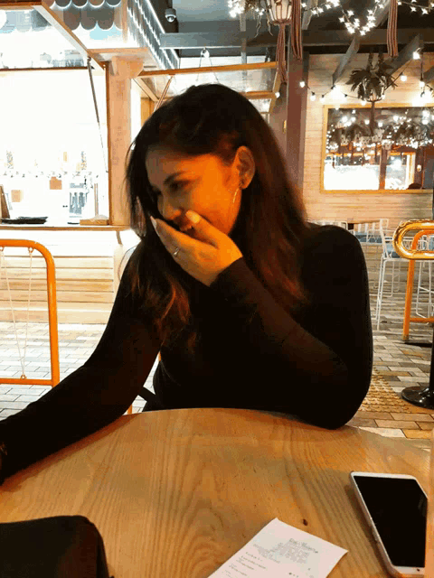 a woman is sitting at a table with her hand over her mouth