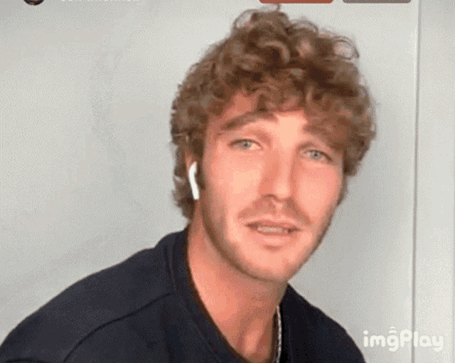 a man with curly hair and a beard is wearing ear buds .