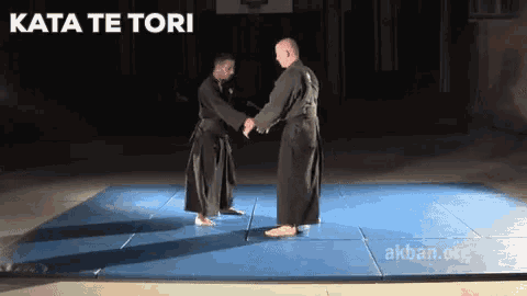 two men shaking hands on a blue mat with the words kata te tori written above them
