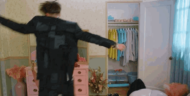 a man is dancing in a room with a closet full of clothes and a dresser .