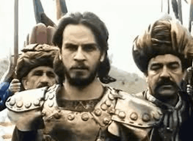 a man in armor and a turban is standing in front of a group of men .