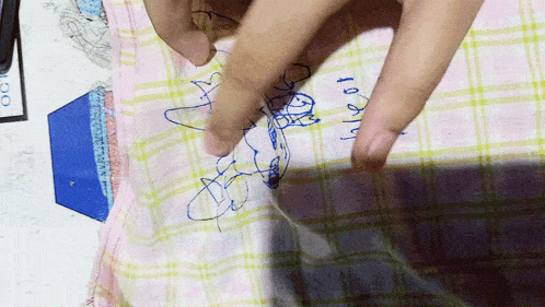 a person is drawing a picture on a plaid cloth with the word hello written in blue