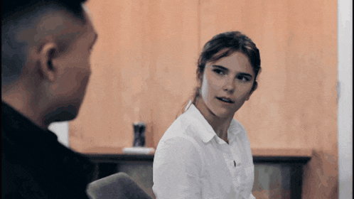 a woman in a white shirt looks at a man in a black shirt
