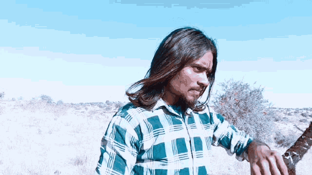 a man with long hair and a plaid shirt is standing in a field