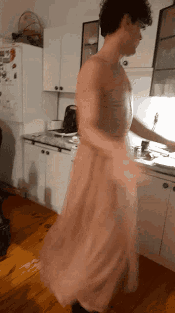 a man in a pink dress stands in a kitchen