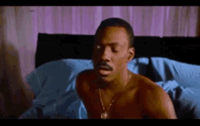 a shirtless man is laying on a bed with blue sheets .