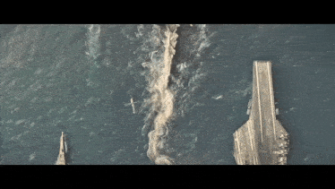 an aerial view of a large aircraft carrier in the ocean with a plane flying overhead