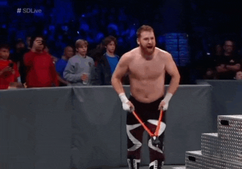 a shirtless wrestler is holding a pair of scissors in front of a crowd of people .