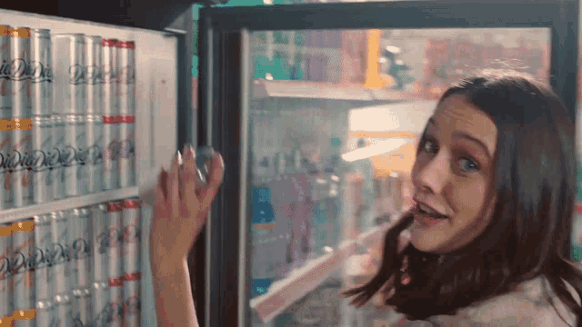 a woman is standing in front of a fridge full of soda cans that say diet coke