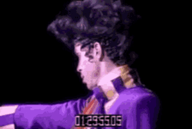 a man in a purple suit and tie is standing on a stage in the dark .