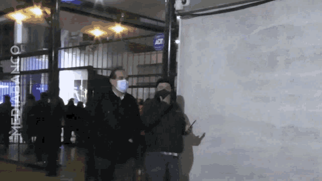 a man wearing a mask stands in front of a sign that says media banco