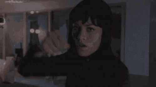 a woman in a black jacket is pointing at something in a dark room .