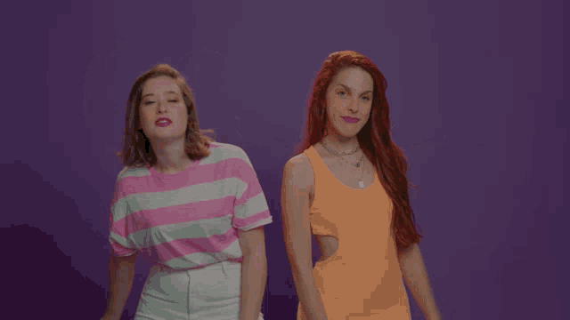 two women are flexing their muscles in front of a purple backdrop