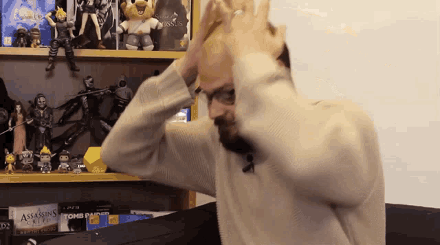 a man holds his head in front of a shelf full of action figures including a tomb raider box