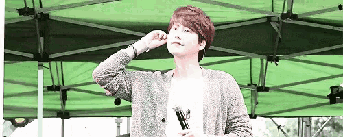 a man is standing under a green tent holding a microphone and adjusting his hair .