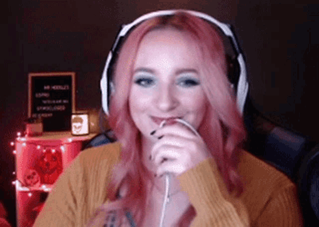 a woman with pink hair is wearing headphones and smiling while sitting in a chair .