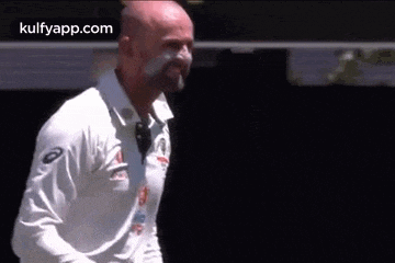 a bald man with white paint on his face is standing in front of a black wall .