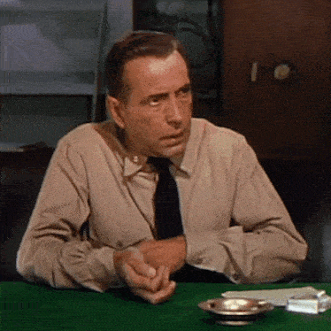 a man in a tan shirt and tie sits at a green table