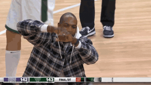 a man in a plaid shirt is making a funny face in front of a scoreboard that says 143 final / ot