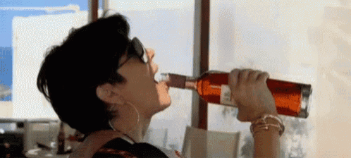 a woman is drinking a bottle of wine from a glass .