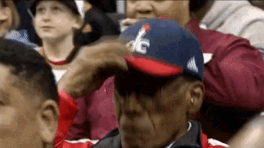 a man wearing a hat with the letter dc on it is sitting in a crowd of people .
