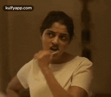 a woman is brushing her teeth with a toothbrush and looking at herself in the mirror .