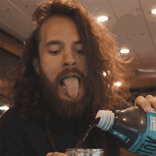 a man with long hair and a beard is drinking from a bottle of aquafina